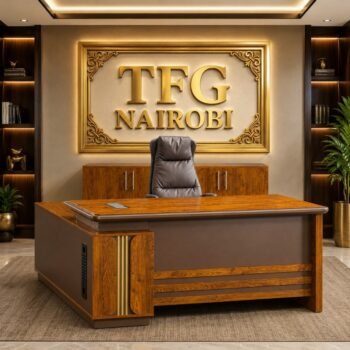 A premium JO1-1.6M Executive Office Desk with a luxury wood finish from HOMEFELT FURNITURE paired with a brown leather high-back chair under a gold TFG NAIROBI sign.