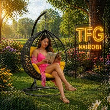 A lady in a pink summer dress reading a magazine while sitting in a black SERENGETI BY188 wicker swing chair with yellow cushions in a lush villa garden near Crystal Mall, Athi River.