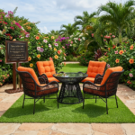 A luxurious BOR400 AMBOSELI Patio Table + 4 Chairs with black rattan chairs, vibrant orange cushions, and a glass-top table, displayed in a beautifully landscaped garden in Mimosa, Runda, Nairobi.