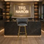 Luxury H-1871 bar chair with high-polished gold legs standing in a premium modern kitchen in Hurlingham under a glowing neon TFG NAIROBI sign.