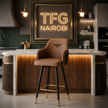 Premium H-1977 LUX bar chair in brown leather with gold accent footrest standing in a luxury apartment kitchen on Arwings Kodhek Road, Hurlingham, under a glowing TFG NAIROBI sign.