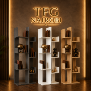 Small Space, Big Style: Why Tree Bookshelves Are the Ultimate Urban Storage Trend in Nairobi. A collection of three premium modern MDF tree-shaped bookshelves from TFG NAIROBI, displayed in dark grey, white, and natural oak finishes. The unique vertical bookcases are styled with globes, books, and busts, set in a luxury luxury office with warm lighting and a discreet golden-bronze "TFG NAIROBI" floor plaque.